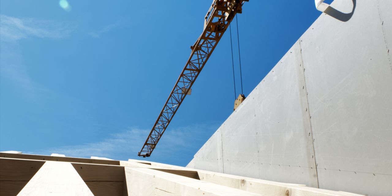 Neuer Holzbalken auf der Wand des Dachgeschosses, dahinter ein Baukran vor blauem Himmel.