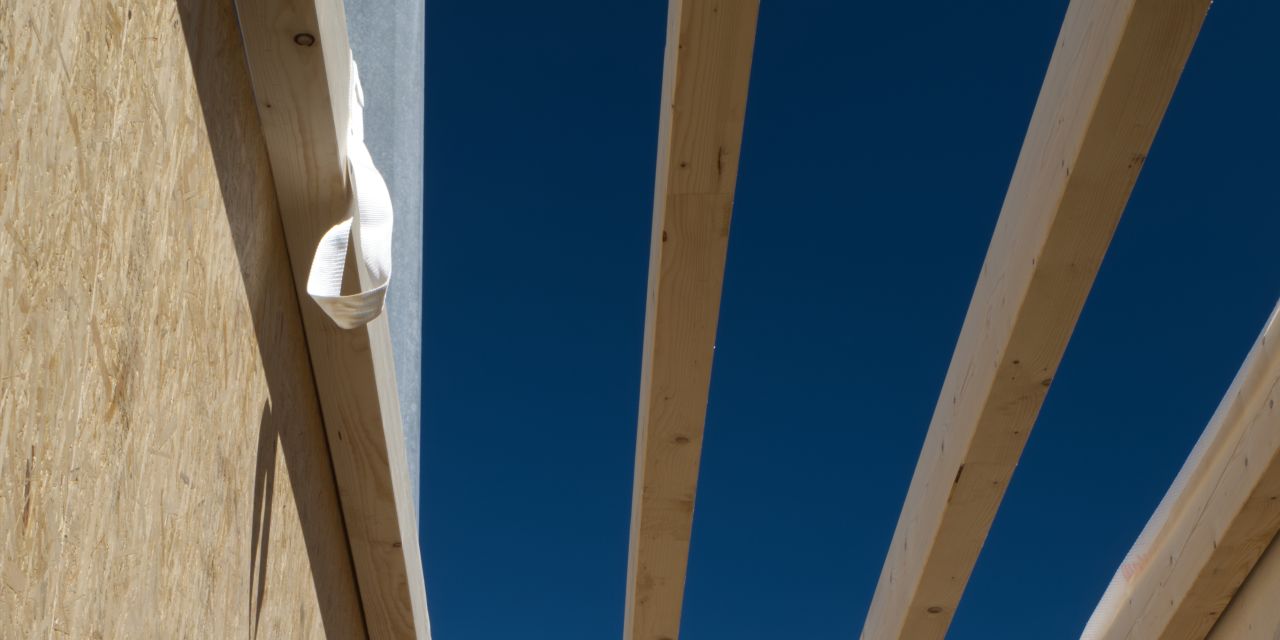 Neue Wände aus Holzständern und OSB-Platten, darüber offene Deckenbalken vor blauem Himmel.